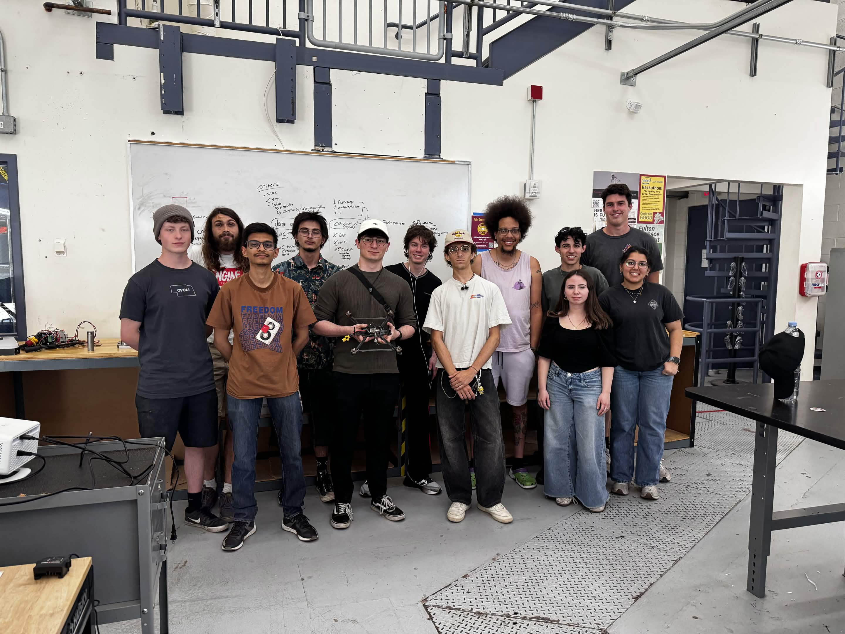 Drone Devils members gathered in the lab holding a custom FPV quadcopter